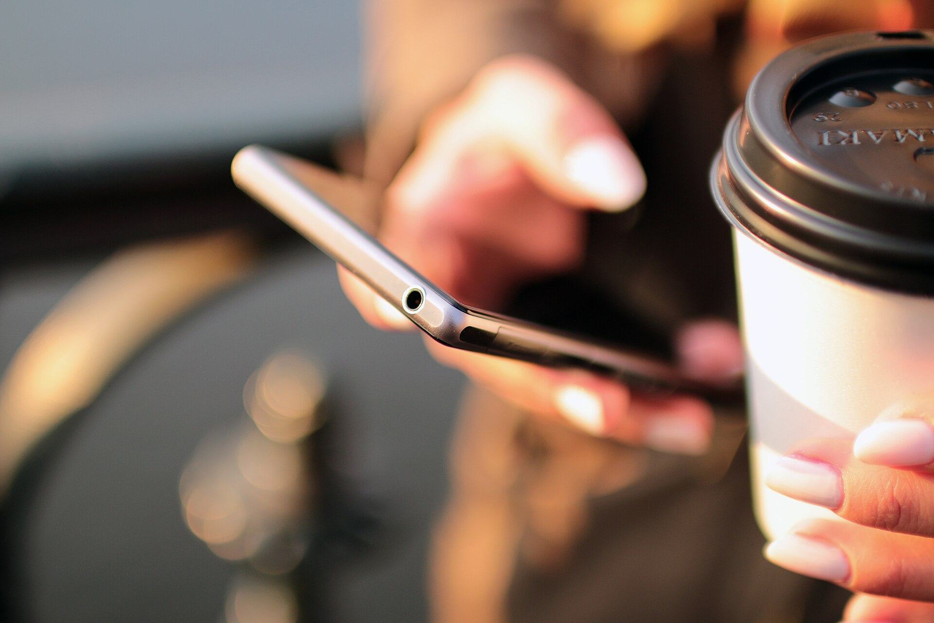 Mãos segurando um celular e um copo de café